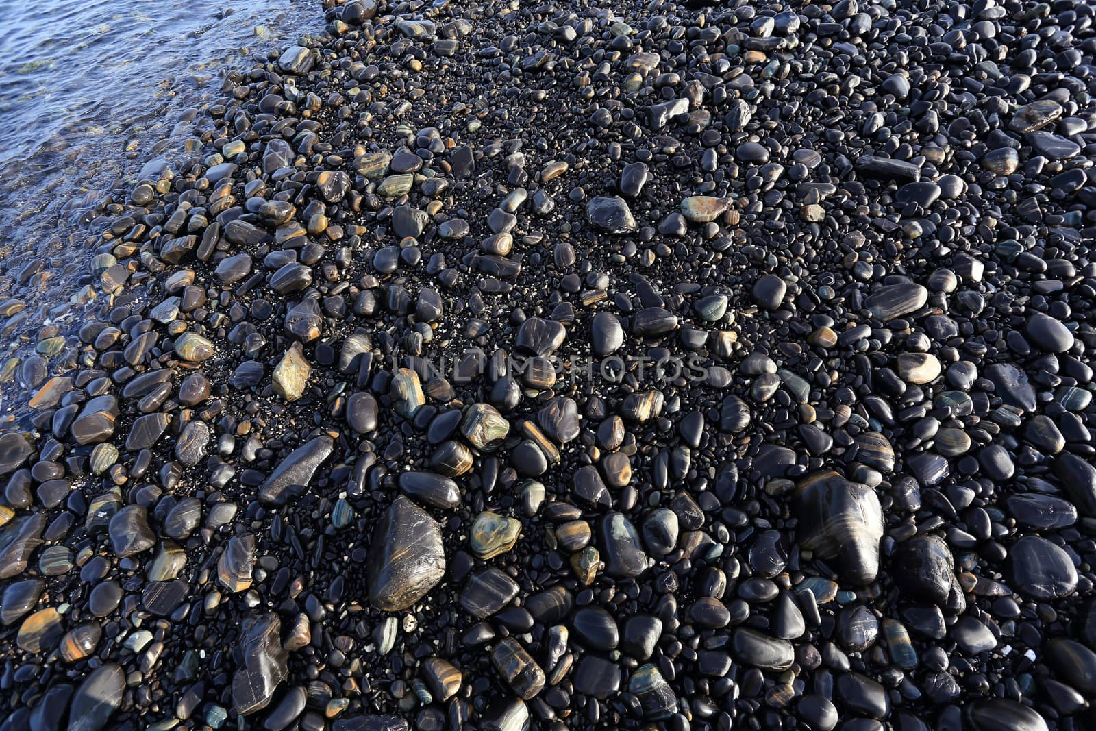 Colorful pebbles touching wave at beautiful rock island, called Koh Hin Ngam, near Lipe island, Thailand