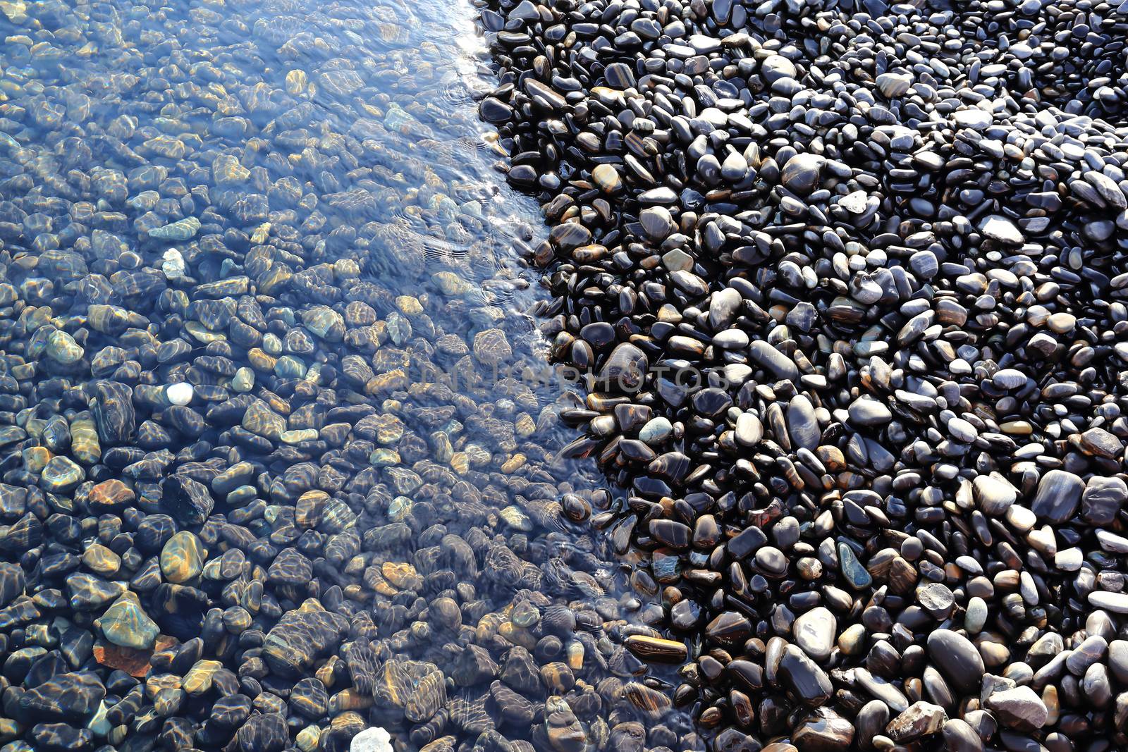 Colorful pebbles touching wave at beautiful rock island, called Koh Hin Ngam, near Lipe island, Thailand