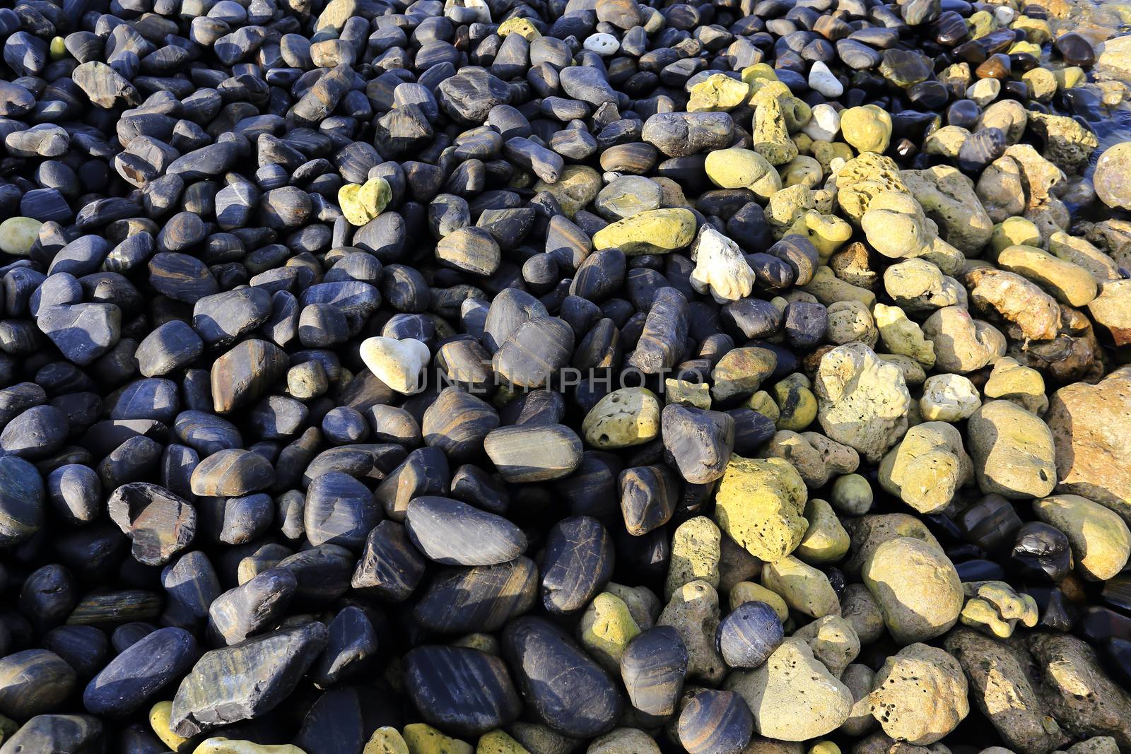 Colorful pebbles touching wave at beautiful rock island, called Koh Hin Ngam, near Lipe island, Thailand