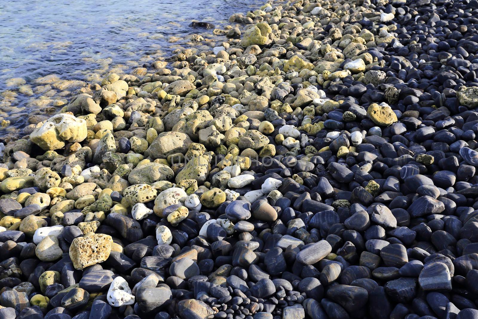 Colorful pebbles touching wave at beautiful rock island, called Koh Hin Ngam, near Lipe island, Thailand