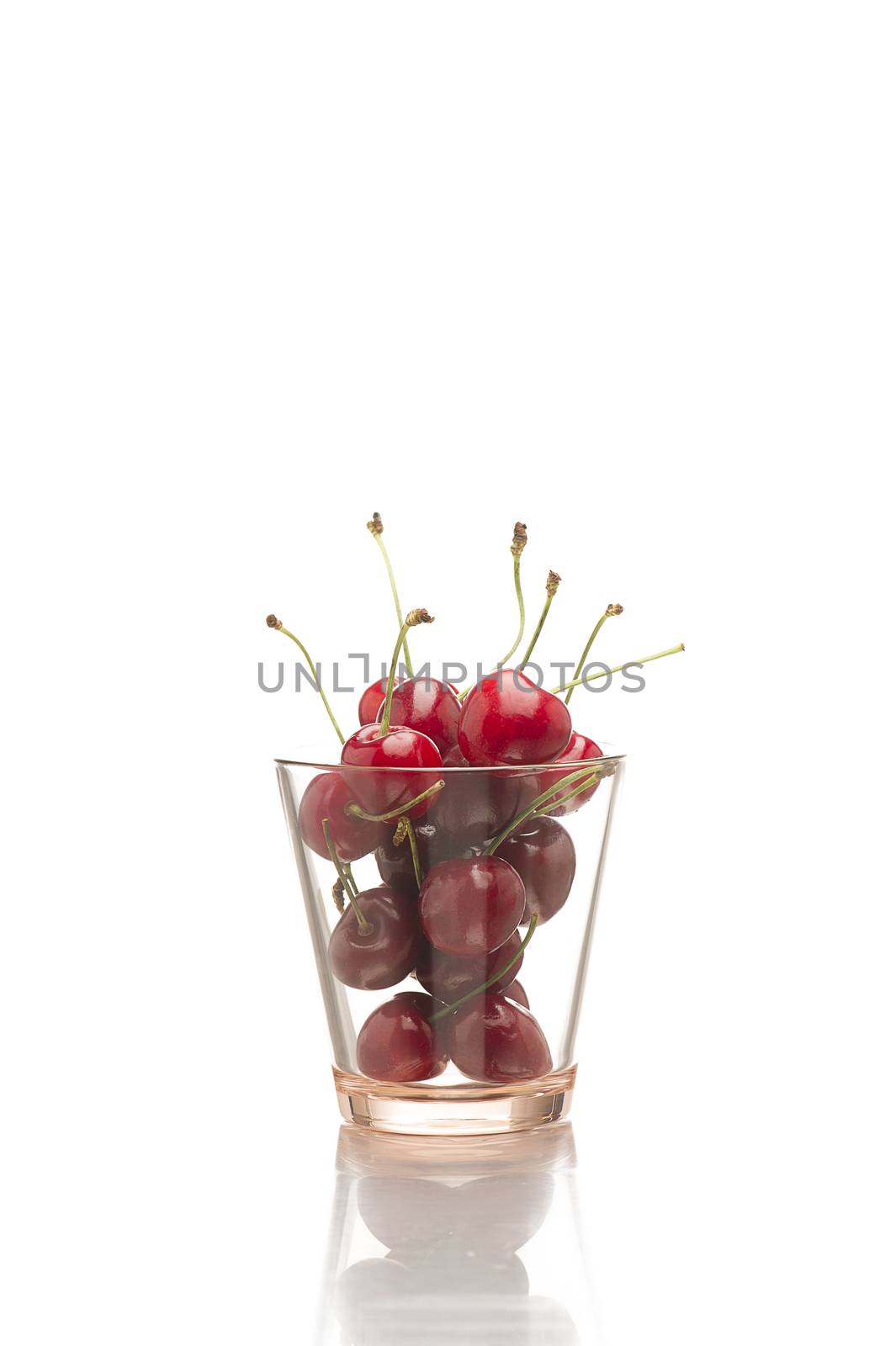 Transparent glass full of luscious ripe red organic cherries rich in Vitamin C, dietary fiber and minerals on a white background with copyspace, vertical format