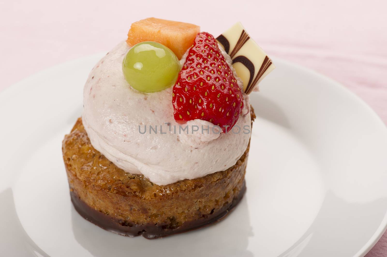 Freshly baked mini cake topped with creamy mousse and fresh tropical fruit with a chocolate wafer served on a plate for dessert or teatime refreshment, with copyspace