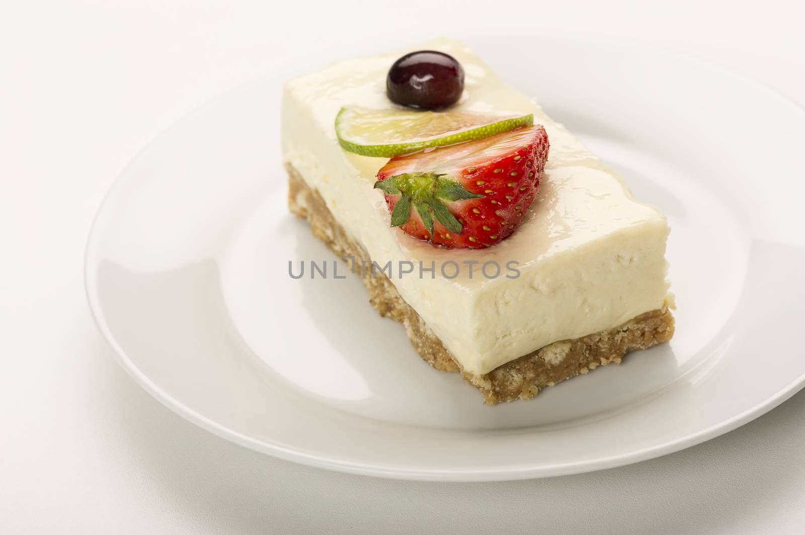 Slice of delicious tangy lemon cheesecake on a biscuit base topped with fresh strawberry and a slice of lemon or lime