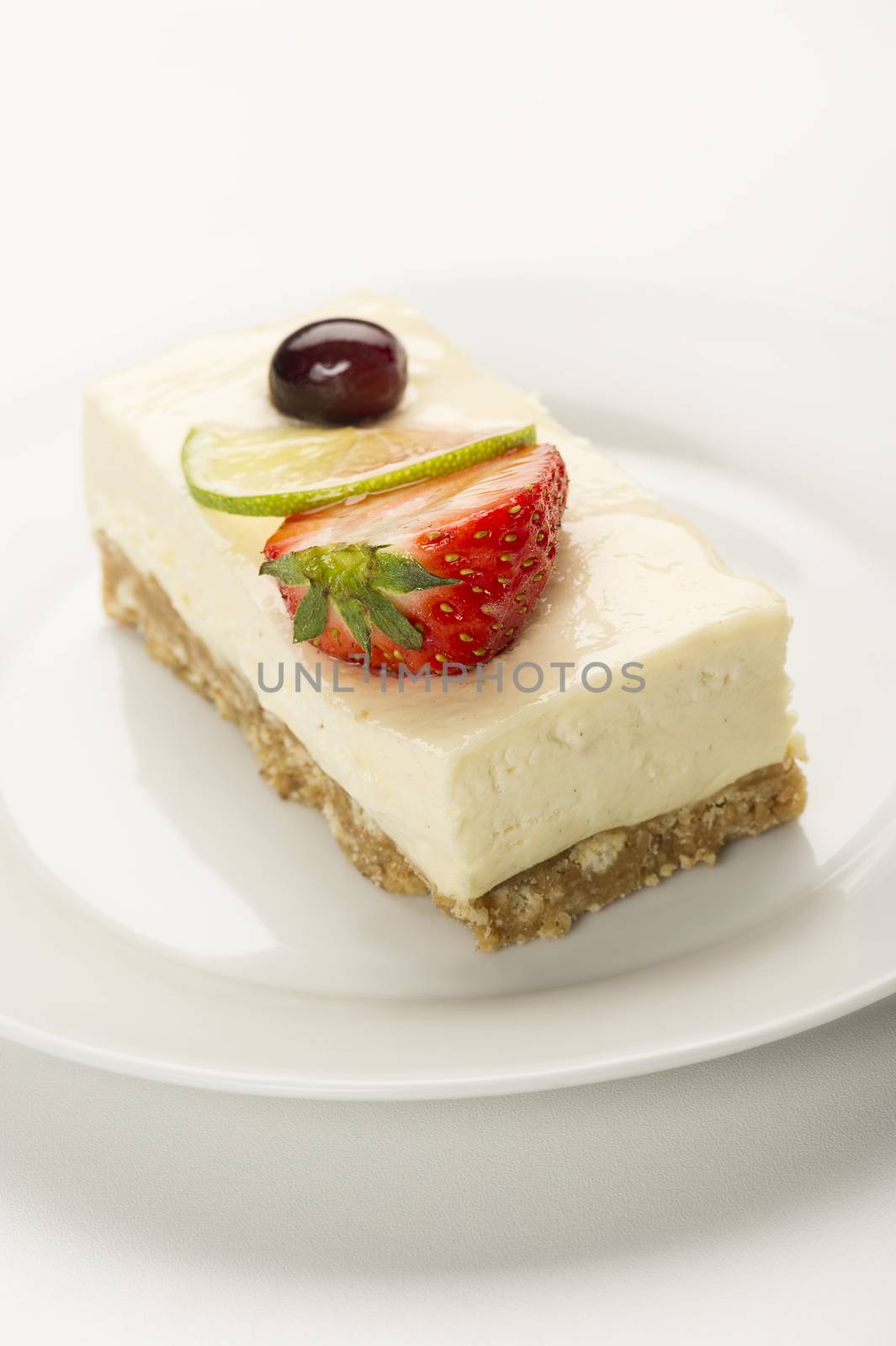 Portion of delicious creamy lemon or lime cheesecake on a pastry base topped with a slice if lime and strawberry , high angle close up view in vertical format with copyspace