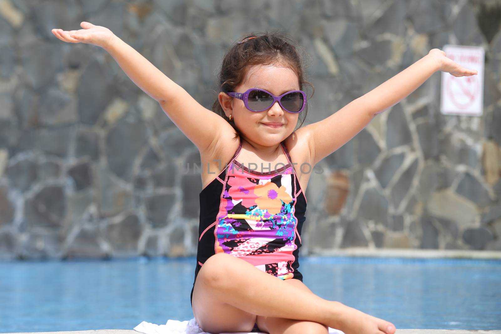 Happy little girl with open arms outside the pool