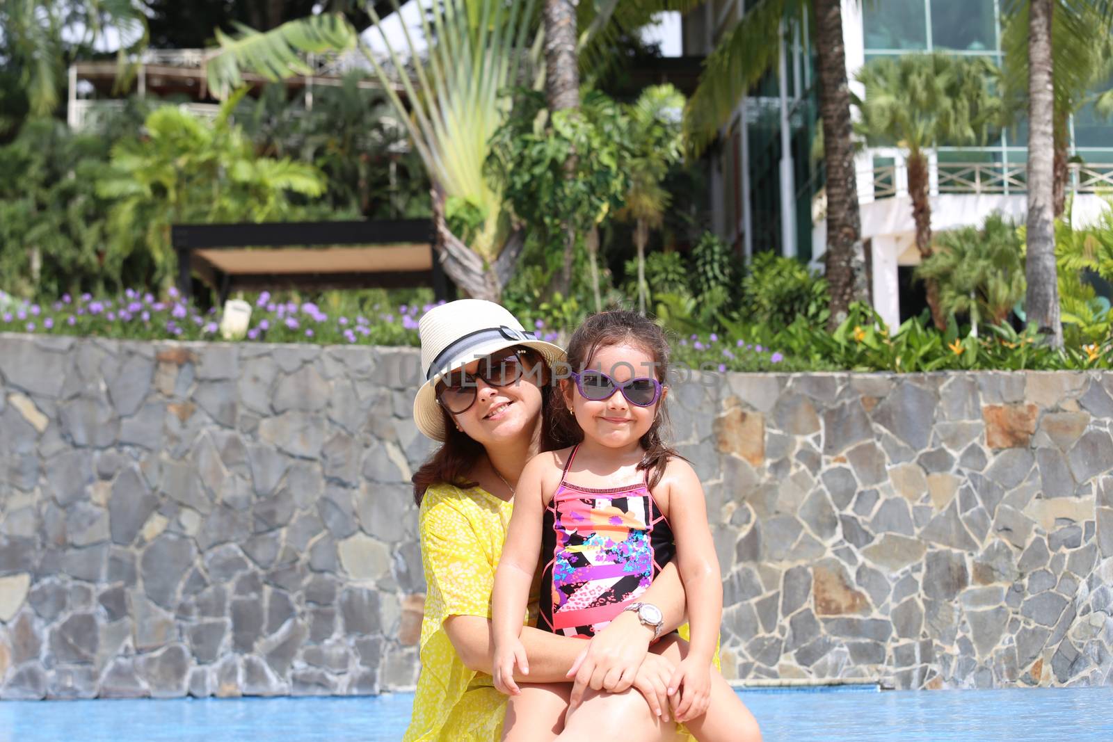 Girl with her mother outside swimming pool enjoying the summerwith their sunglasses