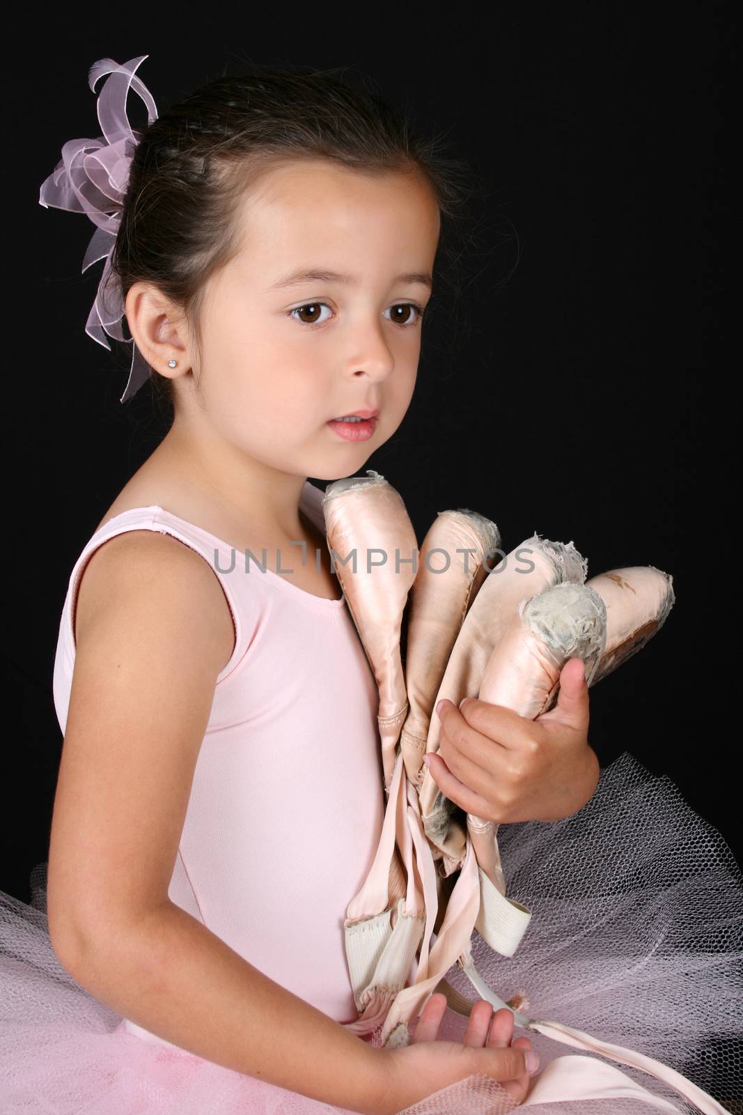 Cute brunette ballet girl holding lots of pointe shoes 