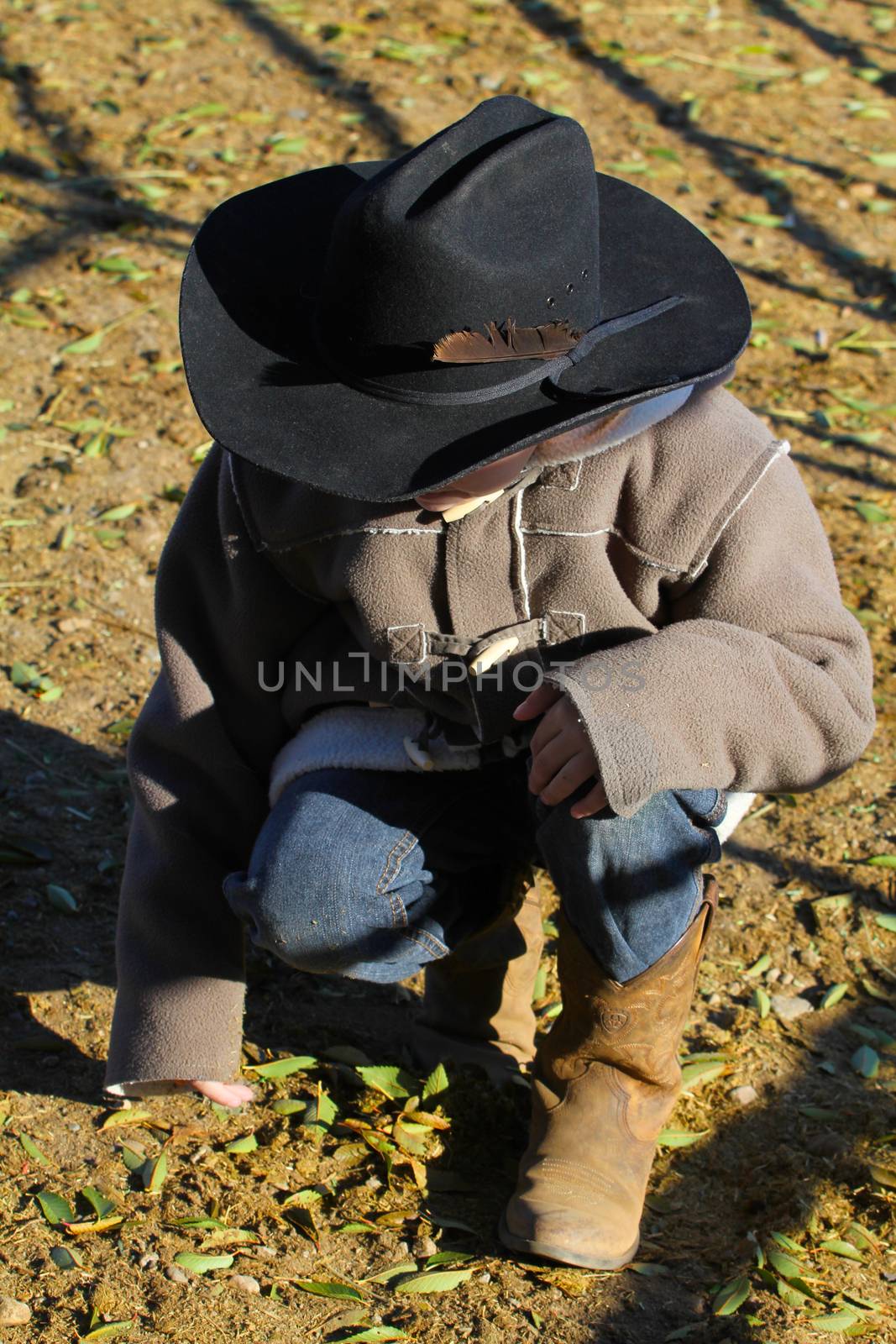 Young cowboy sitting and looking down at dirt