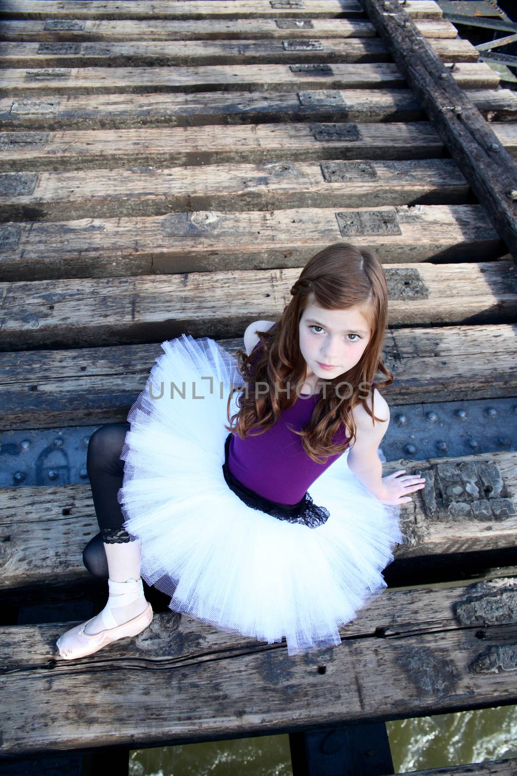 Beautiful girl wearing a white tutu sitting on a bridge