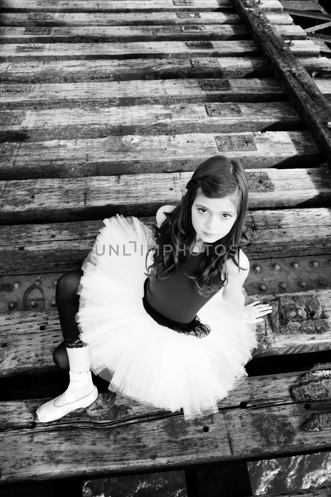 Beautiful girl wearing a white tutu sitting on a bridge