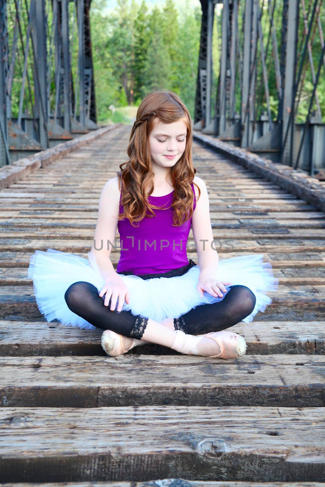 Beautiful girl wearing a white tutu sitting on a bridge