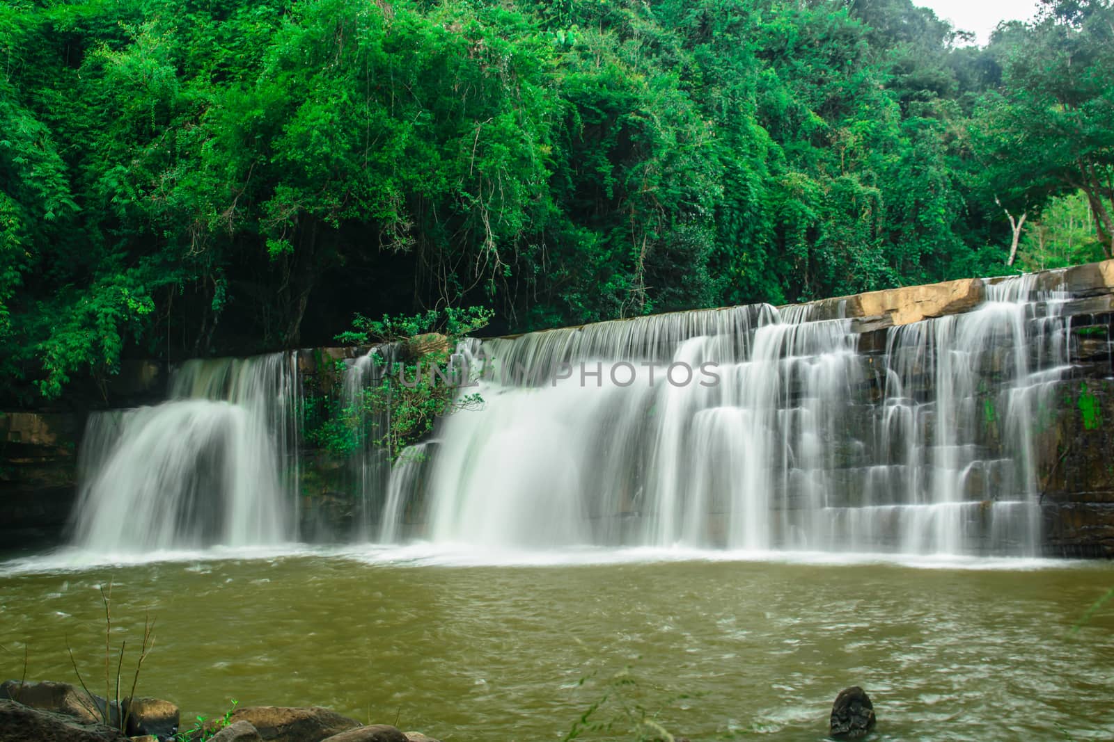 a beautiful waterfall with a green forest on the mountain