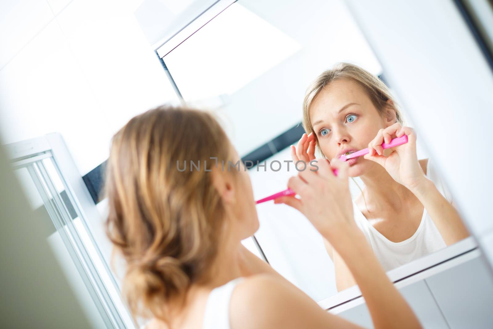 Pretty female brushing her teeth in front of mirror by viktor_cap