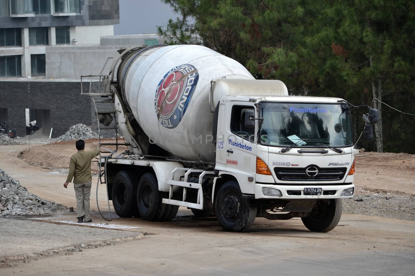 bandung, indonesia-june 9, 2014-indocement concrete mixer truck parking in front of unfinished luxury hotel building