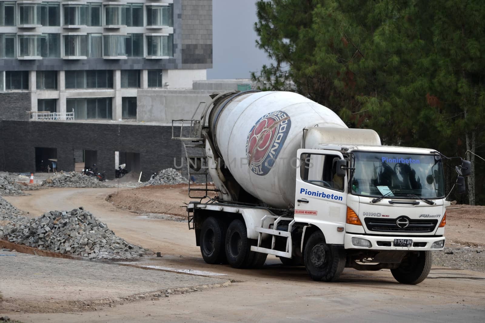 bandung, indonesia-june 9, 2014-indocement concrete mixer truck parking in front of unfinished luxury hotel building
