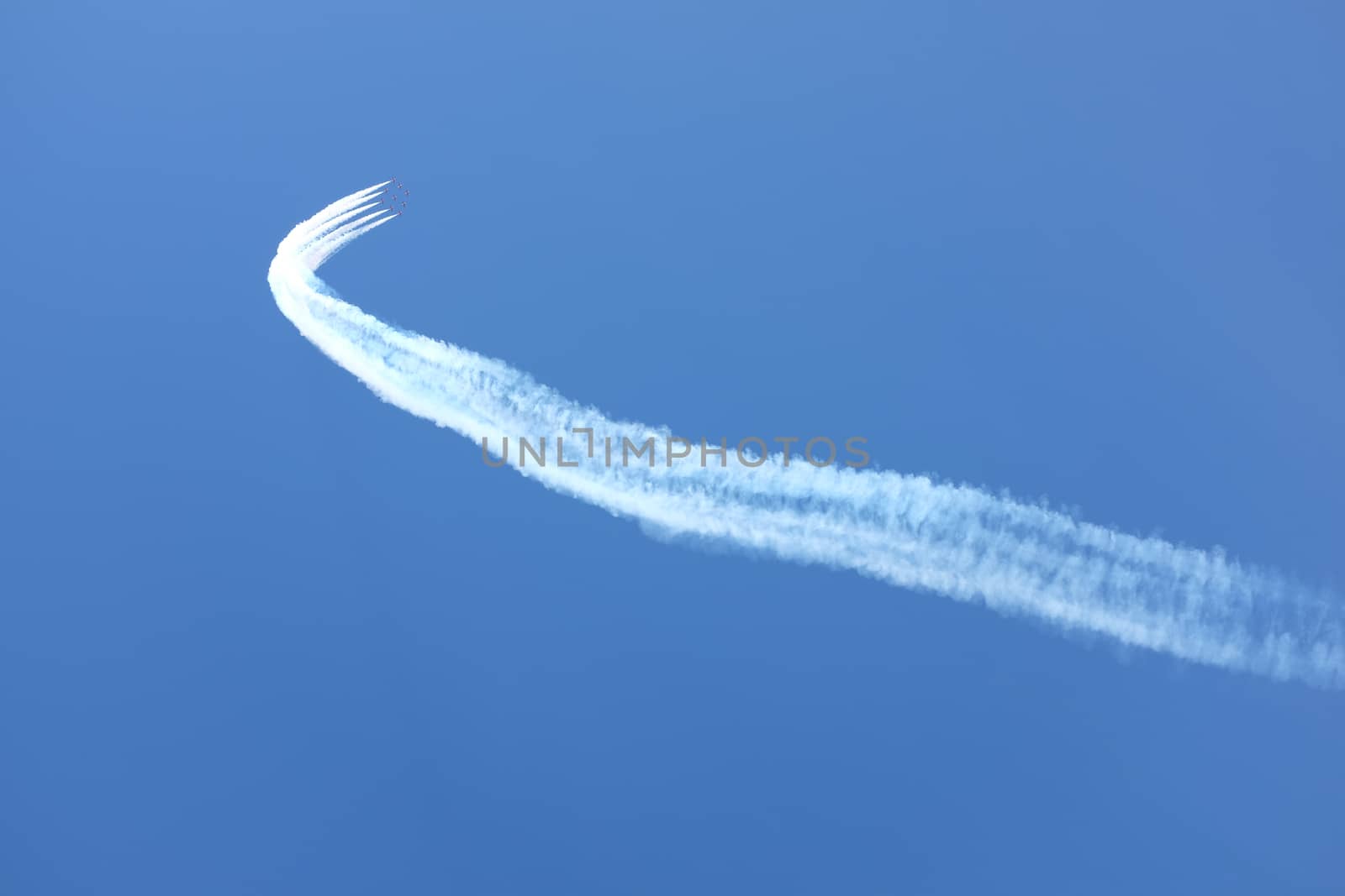 Vapour trails lead to a formation of red jet aircraft in display formation against a clear blue sky.