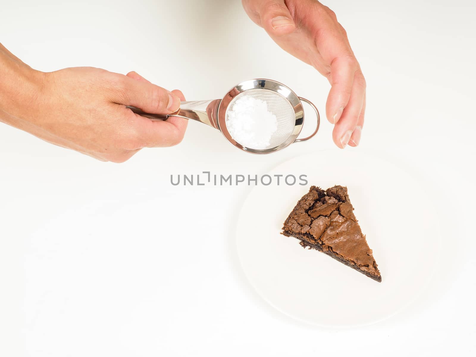 Person adding powdered sugar onto a fresh made chocolate cake with sifter