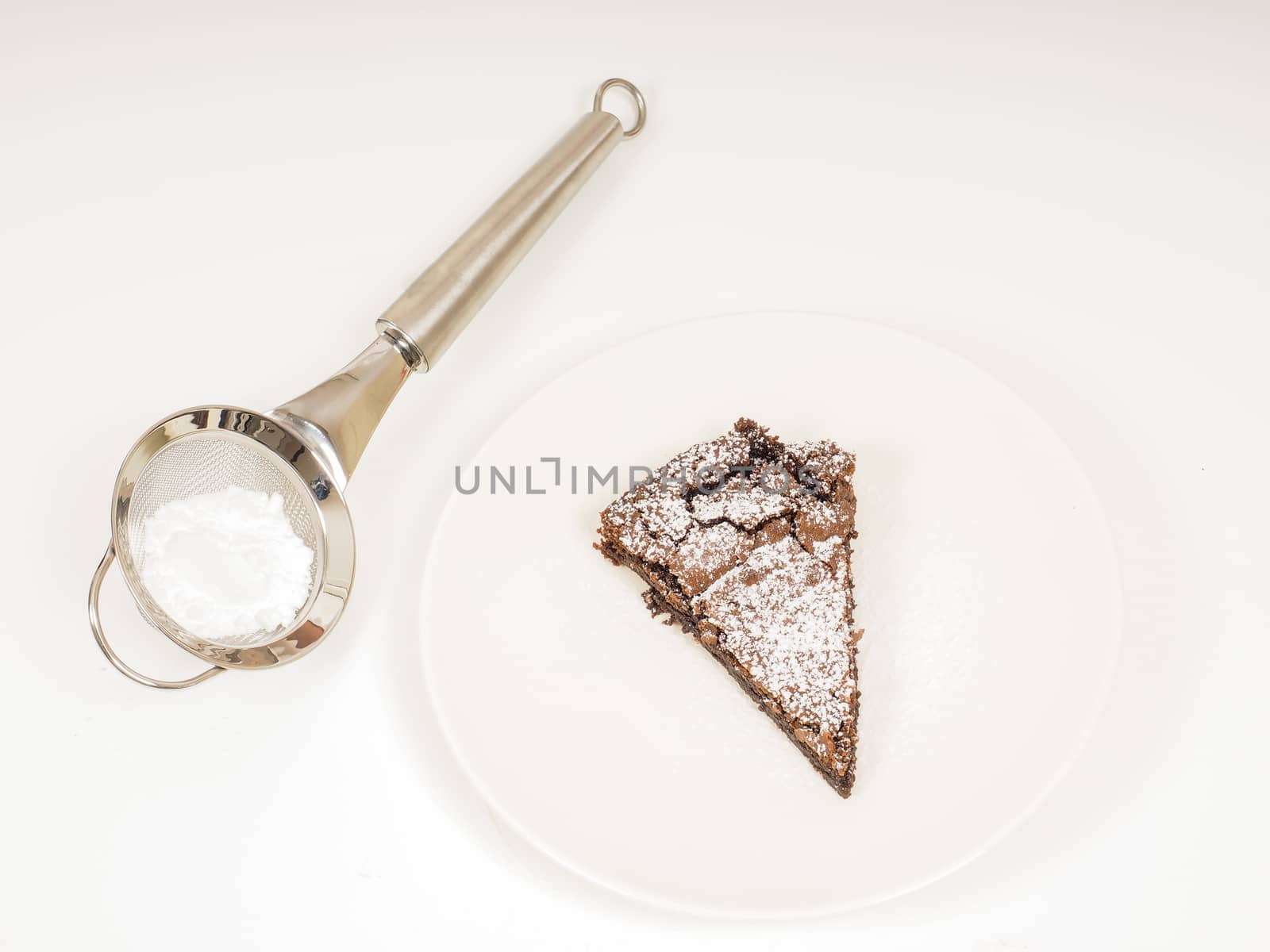 Sifter with powdered sugar next to fresh made chocolate cake