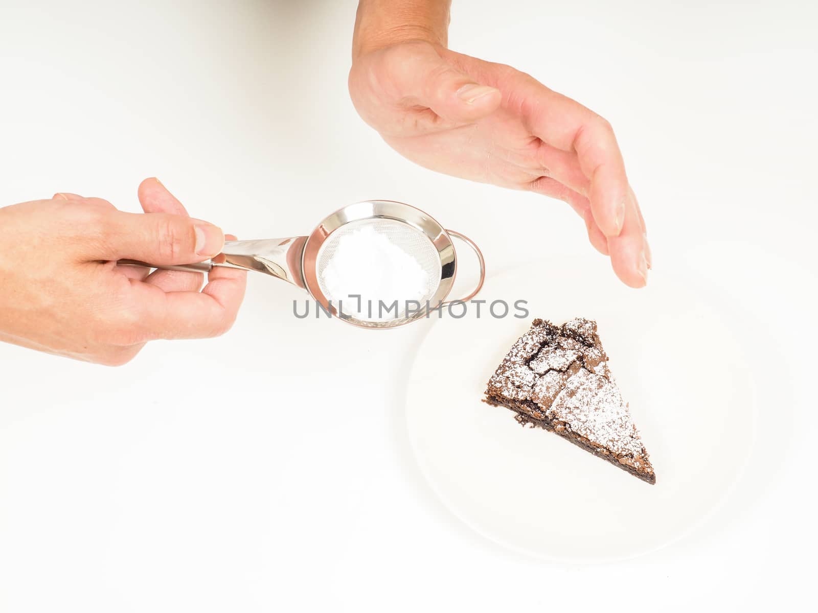 Person adding powdered sugar with sifter onto fresh made chocolate cake