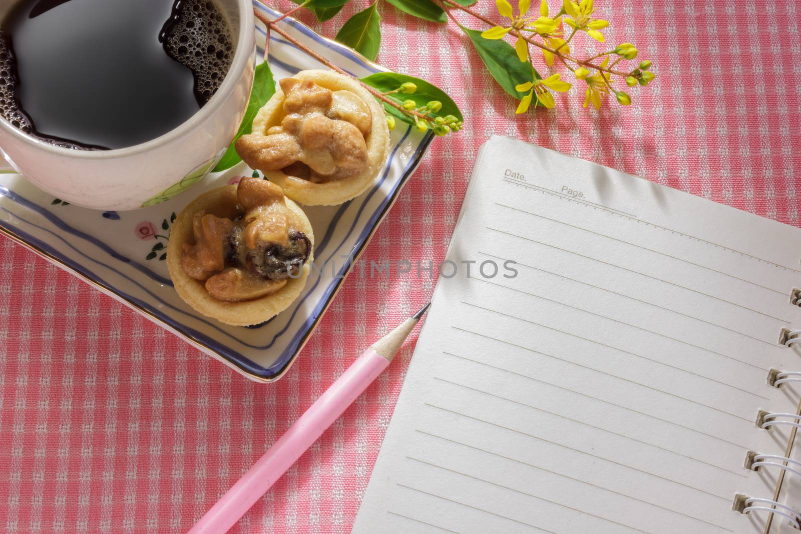 blank notebook on pink cloth table with a cup of coffee and dessert.