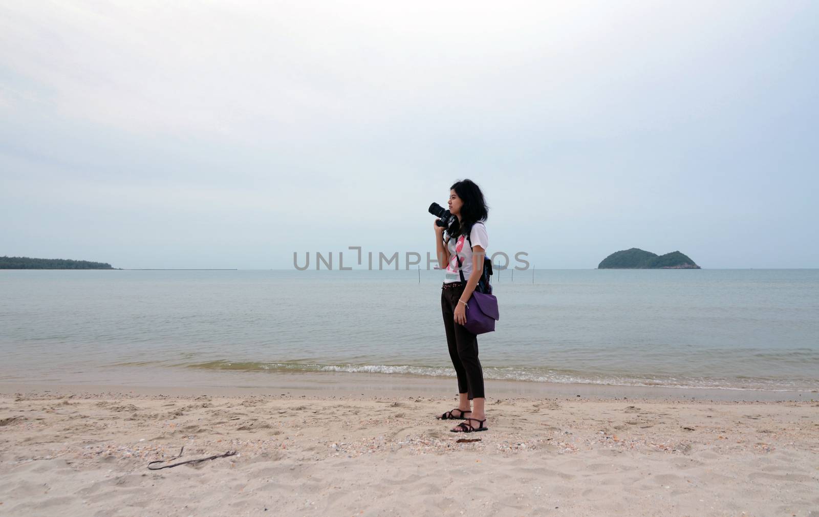 Lonely young woman with camera on the beach by siraanamwong