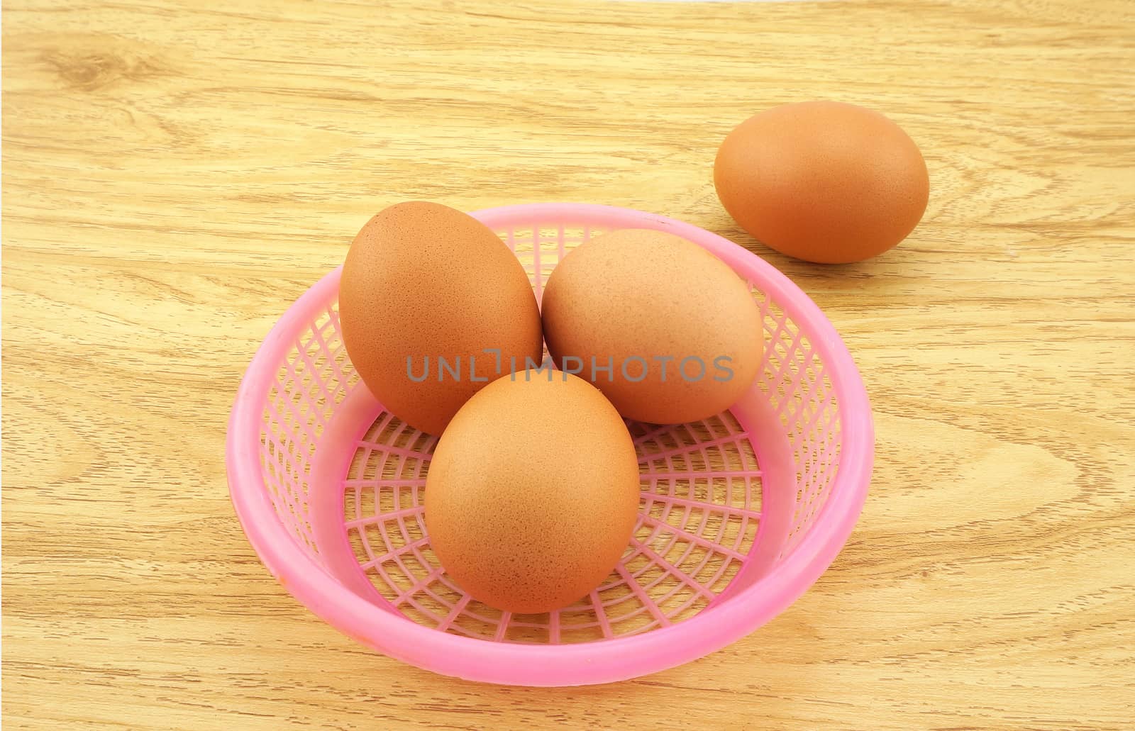 Fresh egg laid on a wooden table. Three eggs in pink basket, another bubble is placed on the outside.                               