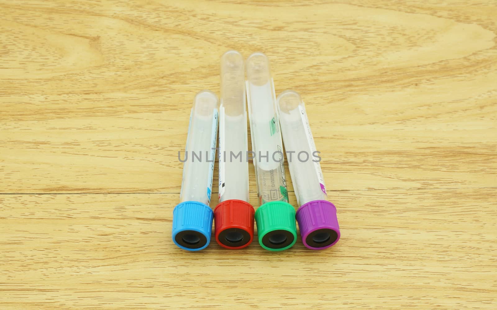 Blood sampling tube put on the wooden table, cap test tubes with four colors: blue, red, green, and purple.                        