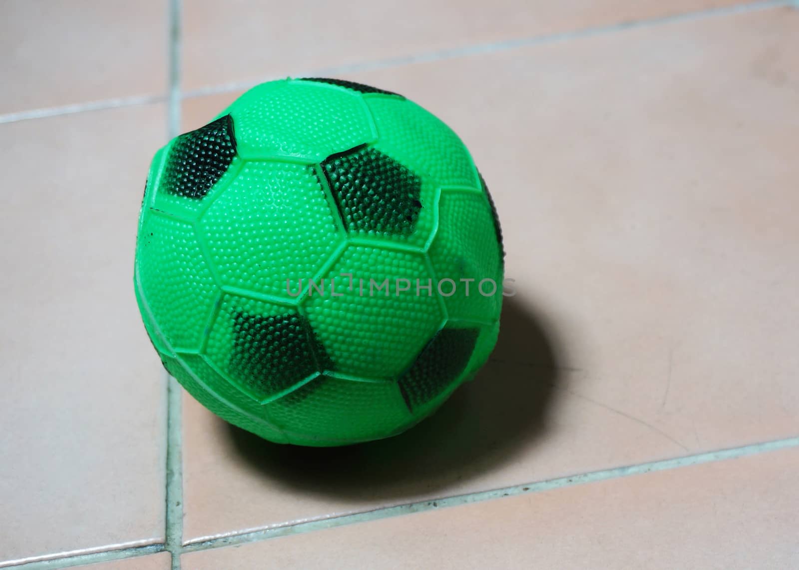 Soccer ball in green color with small black stripes. Placed on the floor at home                              