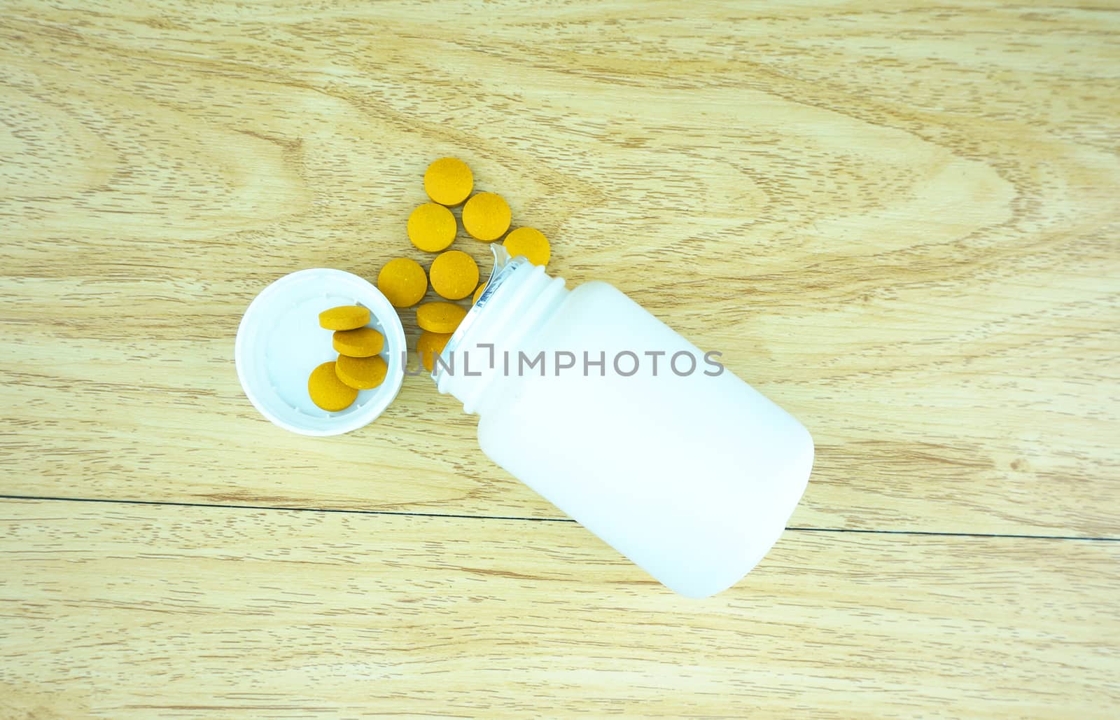 Herbal medicine compressed into tablets, yellow colour, poured out of the white box, put on wooden table.                               