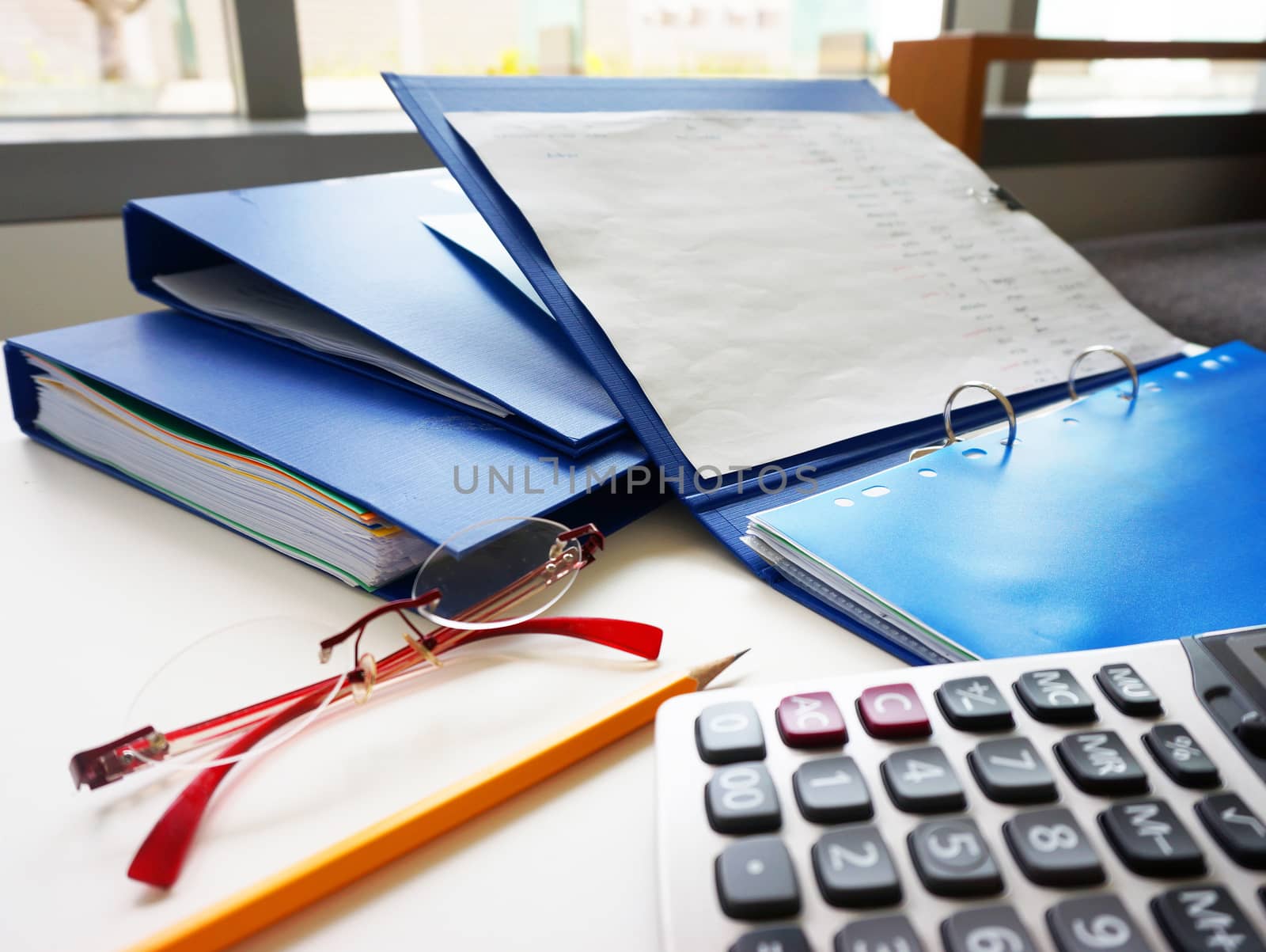 Blue folders and other office equipment, such as calculators, pencil and glasses, placed on the desk.                              