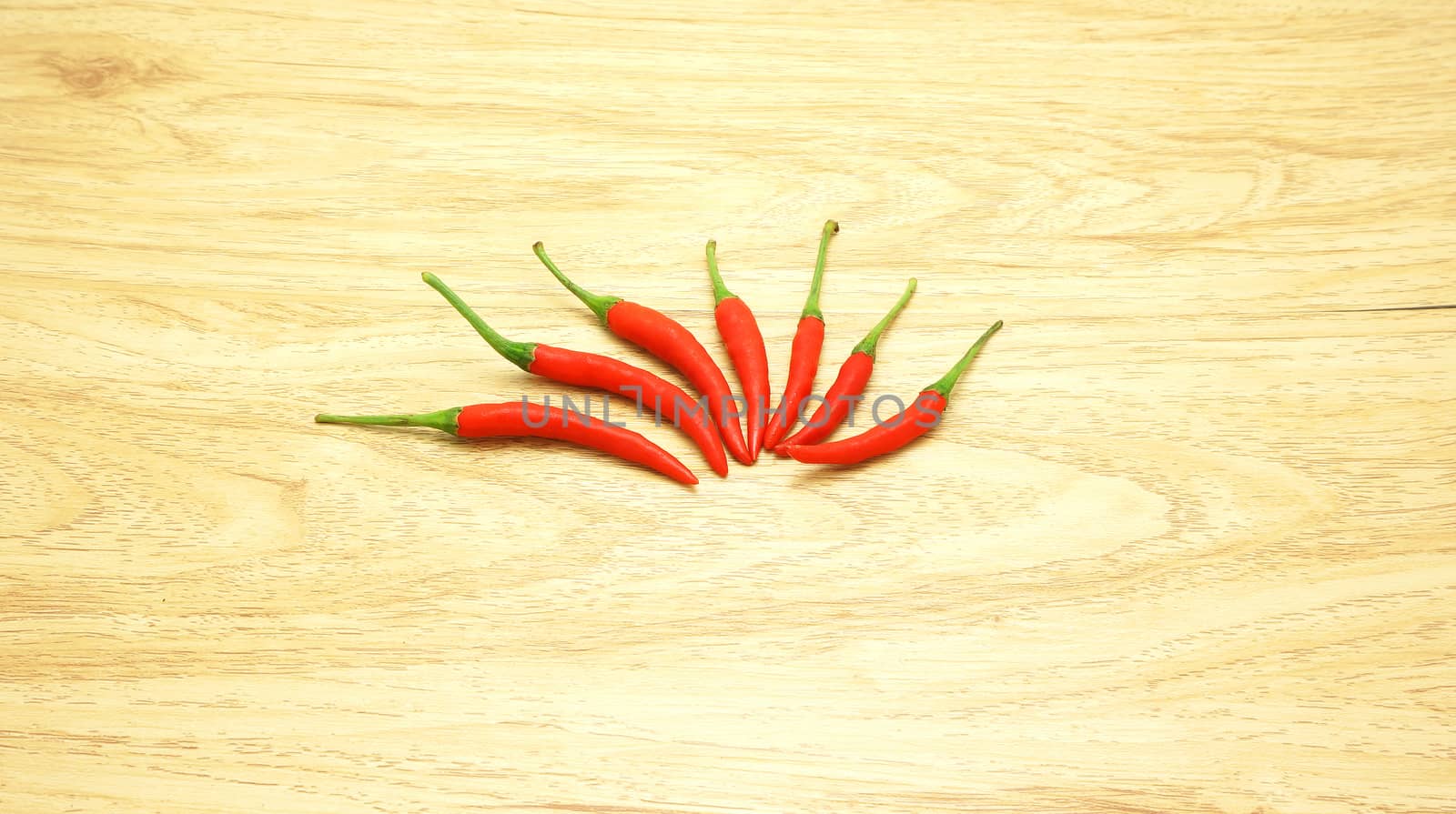 Hot chilli, red fresh and green stalks, lined on the brown wooden table.                             