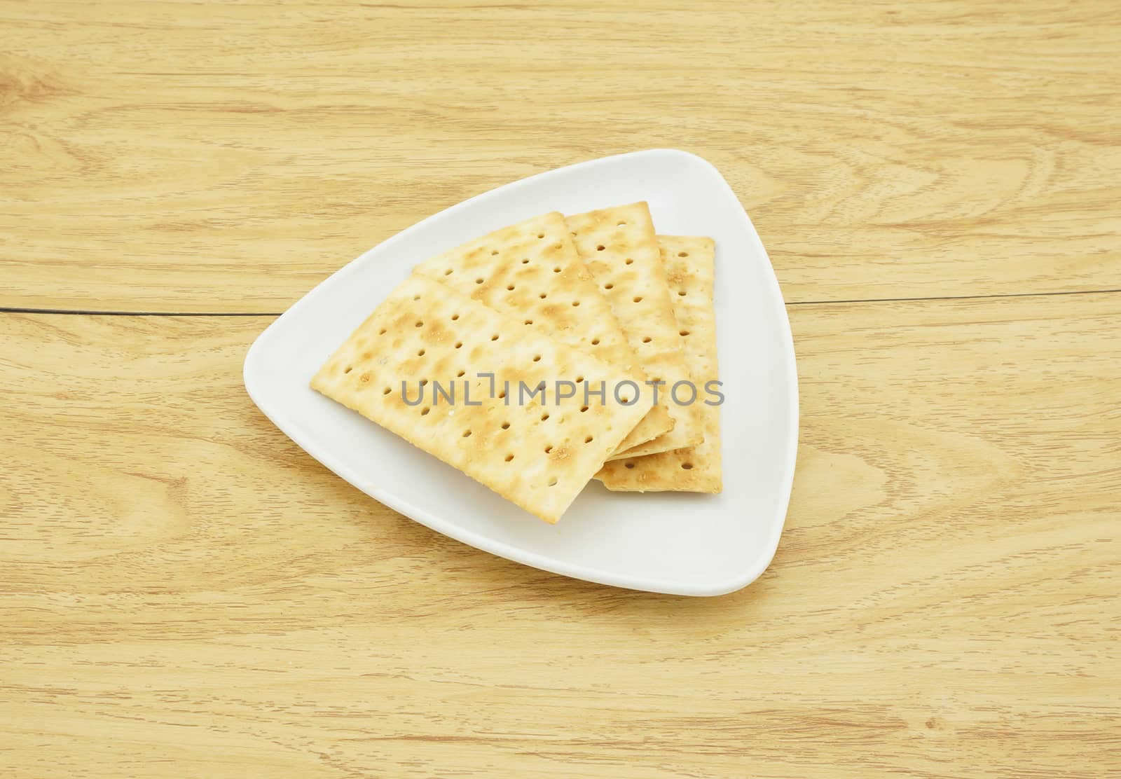 Square crackers in a white plate, put on the wooden table.                            