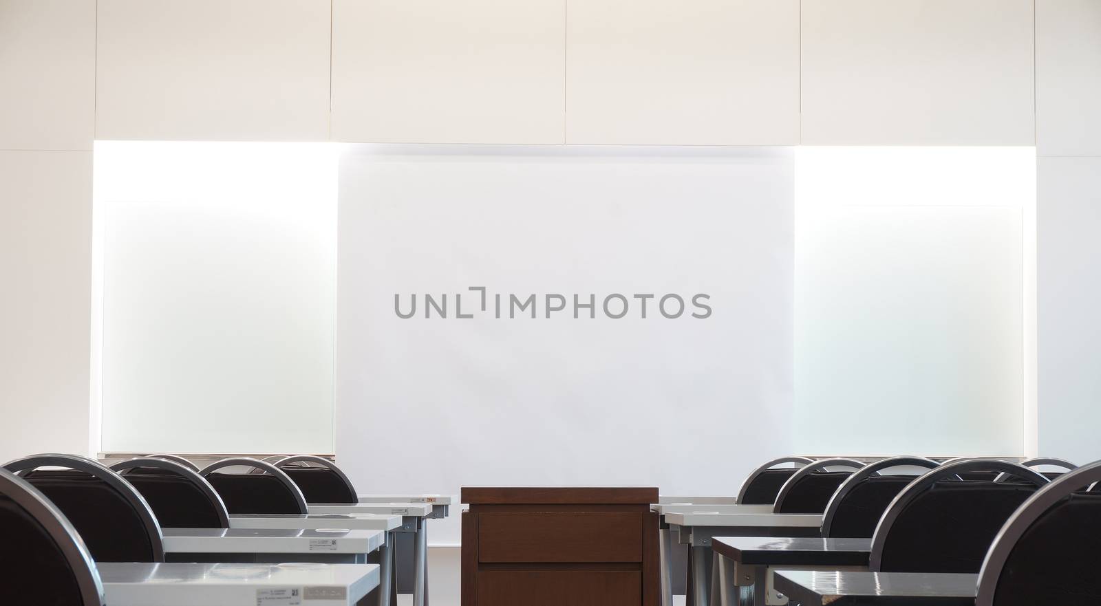 Classrooms on campus have a white background instead of a chalkboard, a desk, a chair and a table in the middle for placing overhead.                              