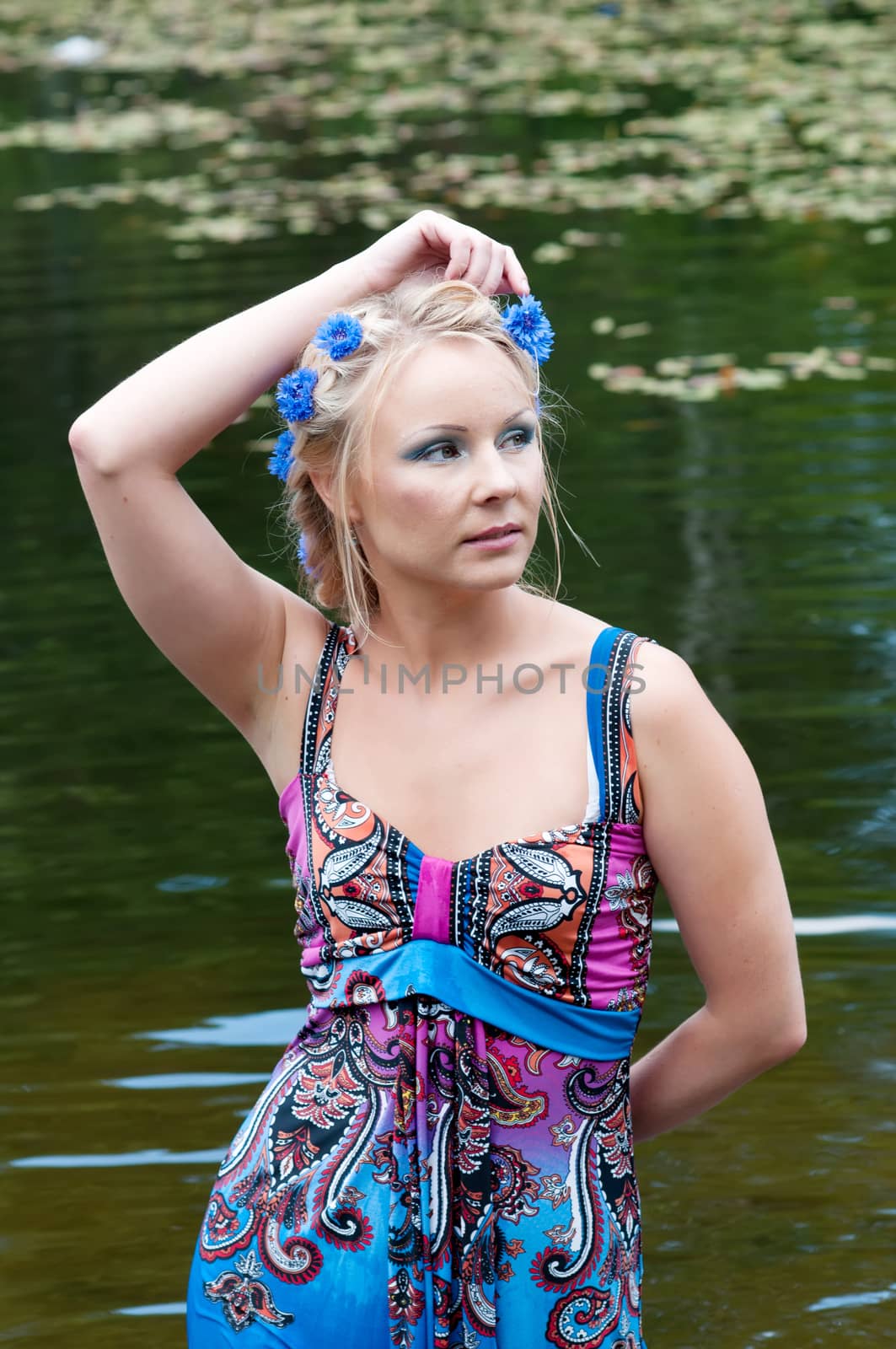 Beautiful blond woman in dress standing near the pond