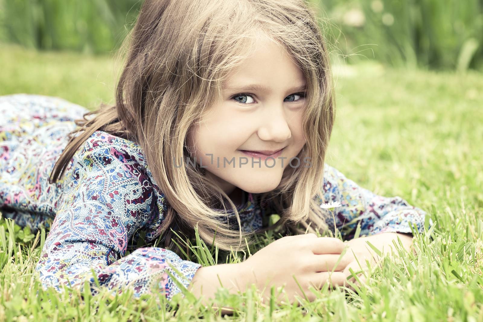 adorable girl lying on grass looking at daisy