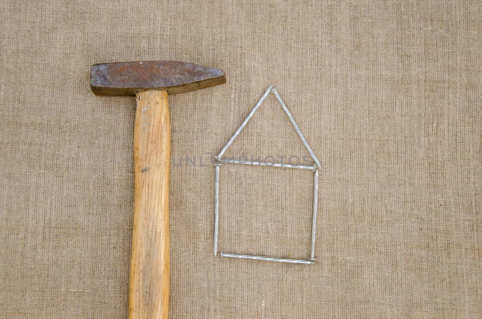 old rusty hammer and house made ??of nails on linen texture