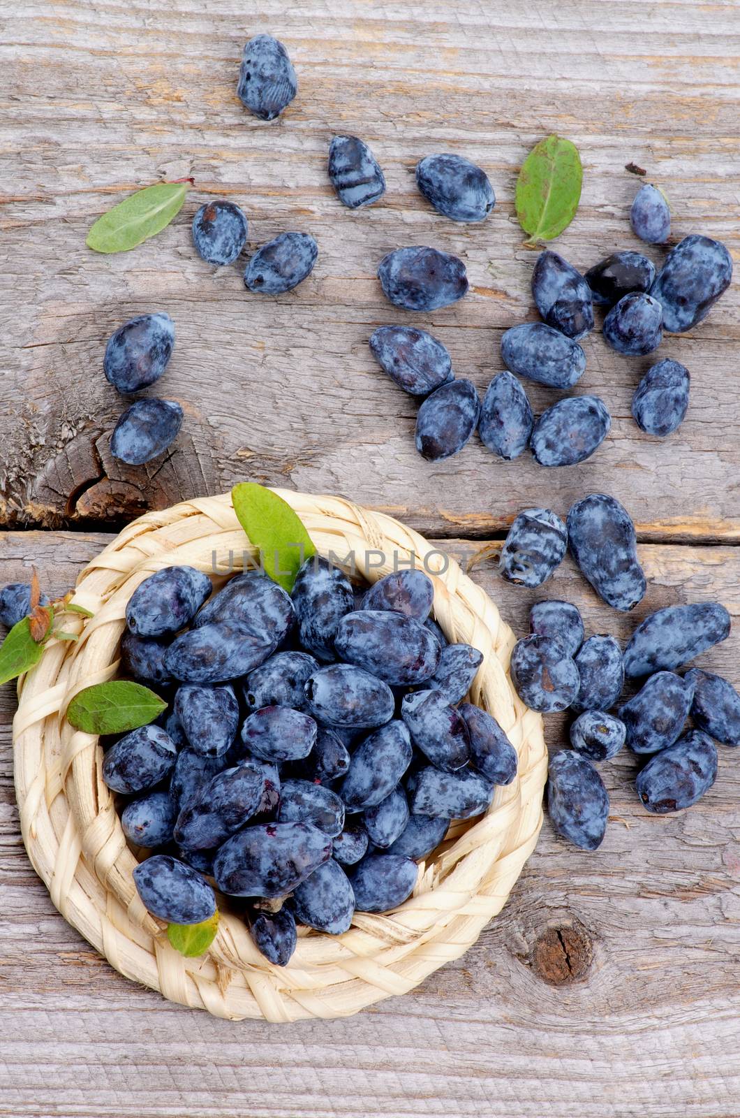 Fresh Ripe Honeysuckle Berries in Wicker Bowl on Rustic Wooden background. Top View