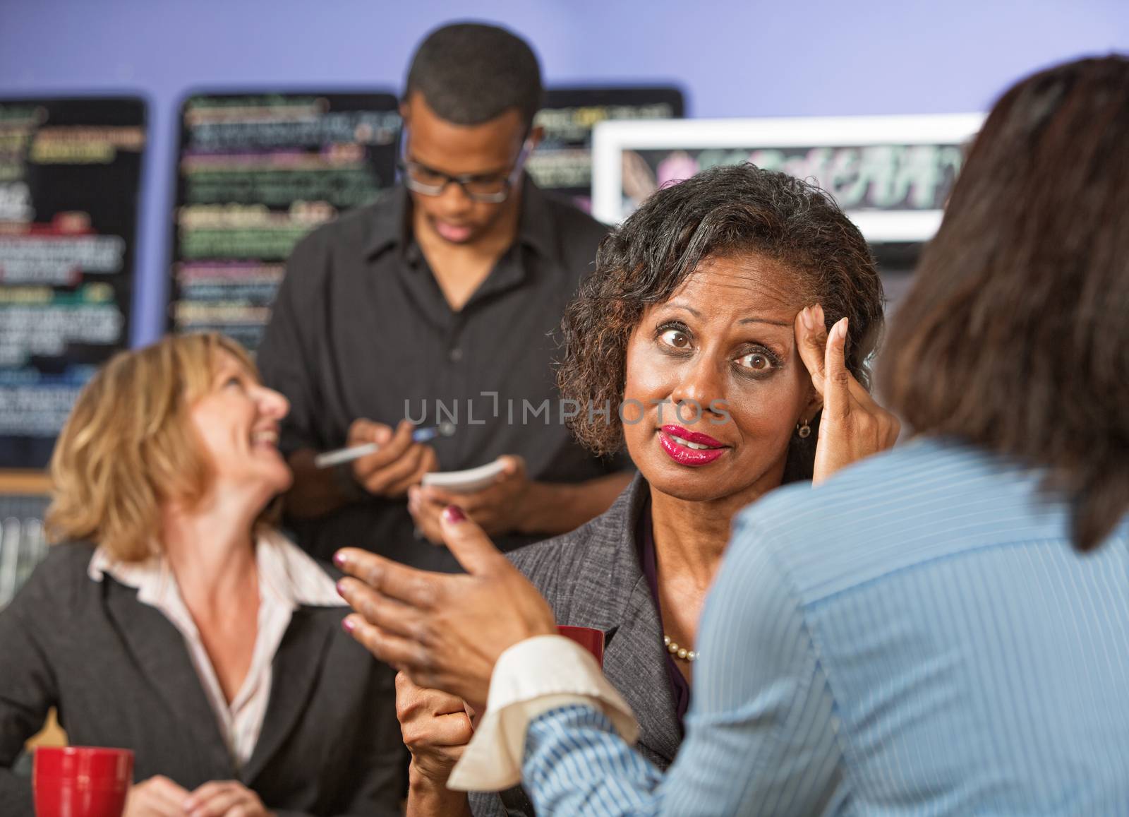 Woman with fingers on head listening to friend in cafe