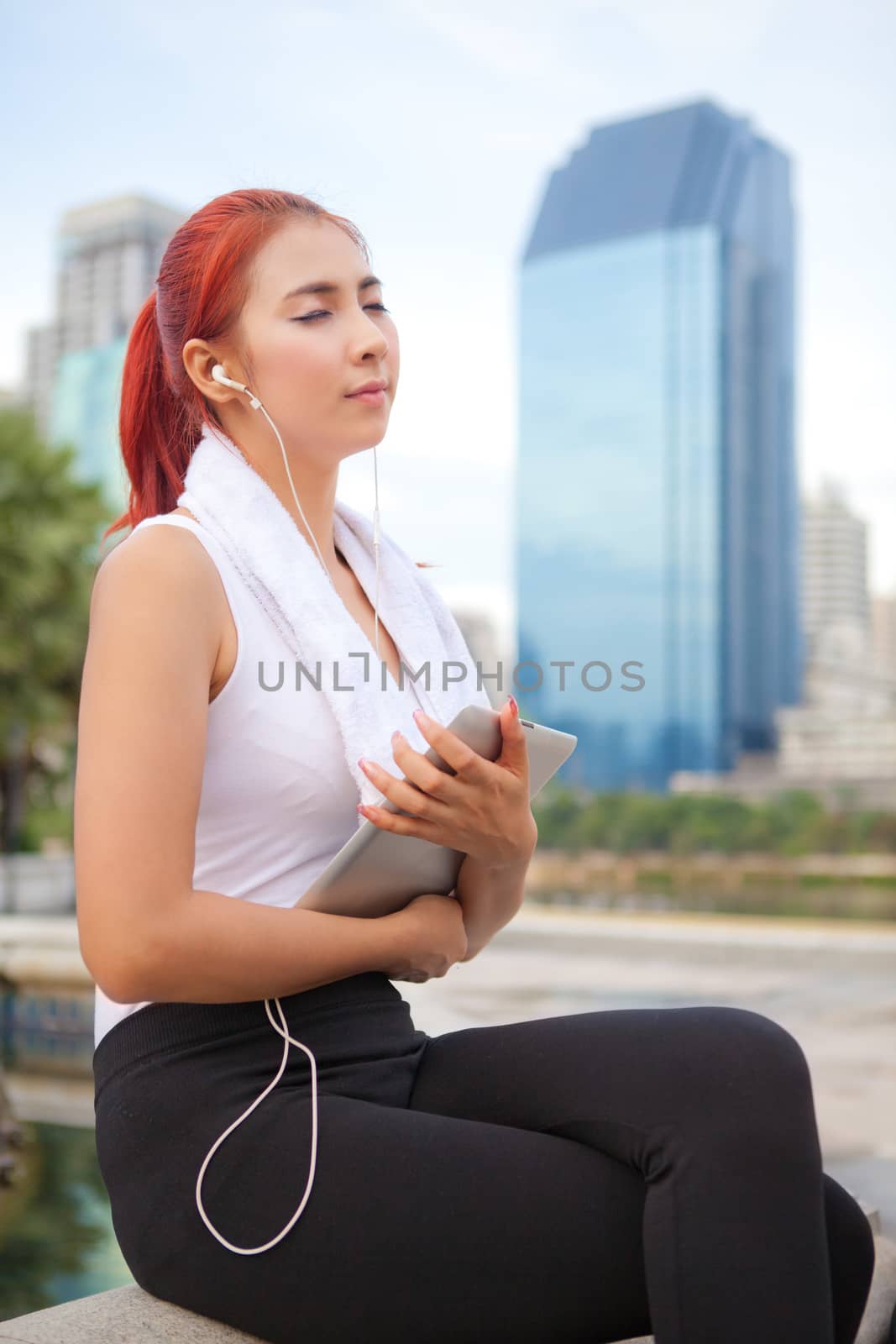 beautiful fitness asian woman listening to music with tablet in park city
