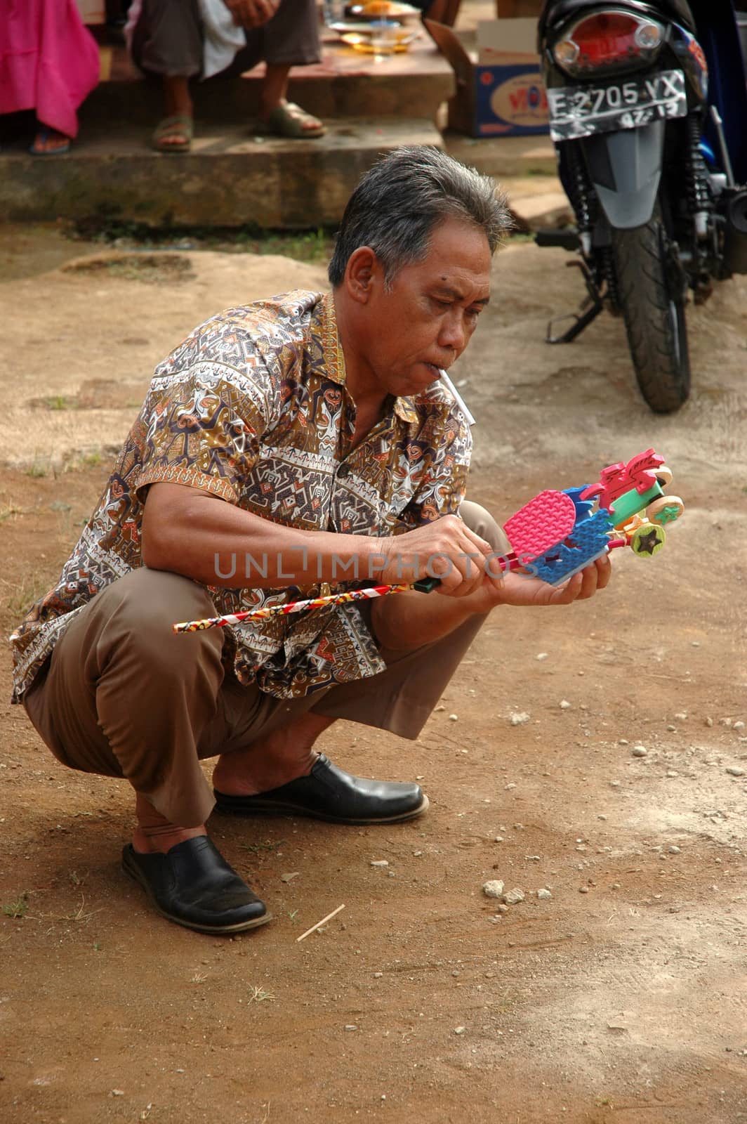 cikijing, west java, indonesia - july 10, 2011: old man holding toy and get smoking