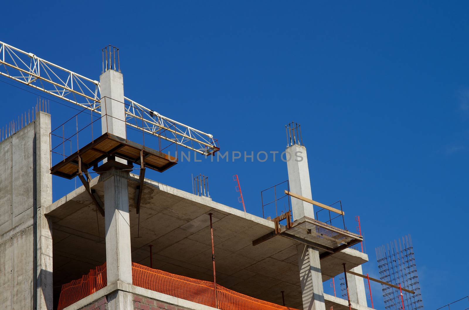 Building Block under Construction with Metal Scaffolding, Concrete Slabs and Construction Crane Towering against Blue Sky