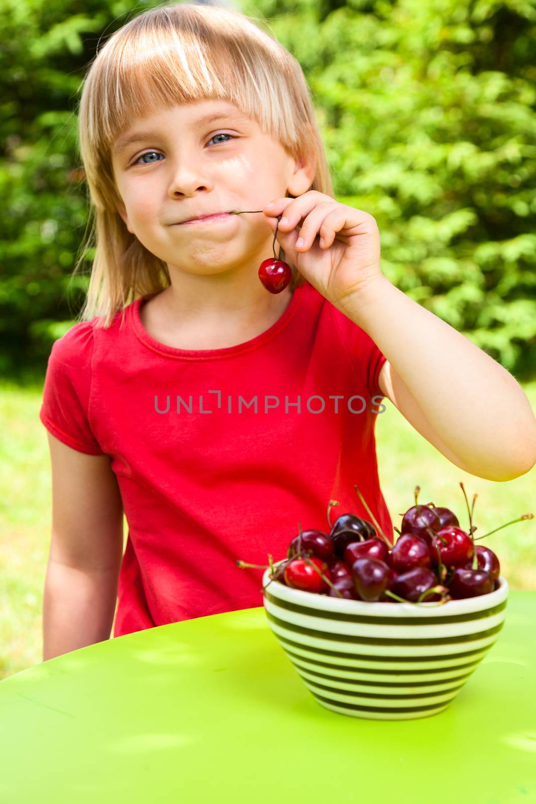 Cute little girl eating sweet cherry outdoors