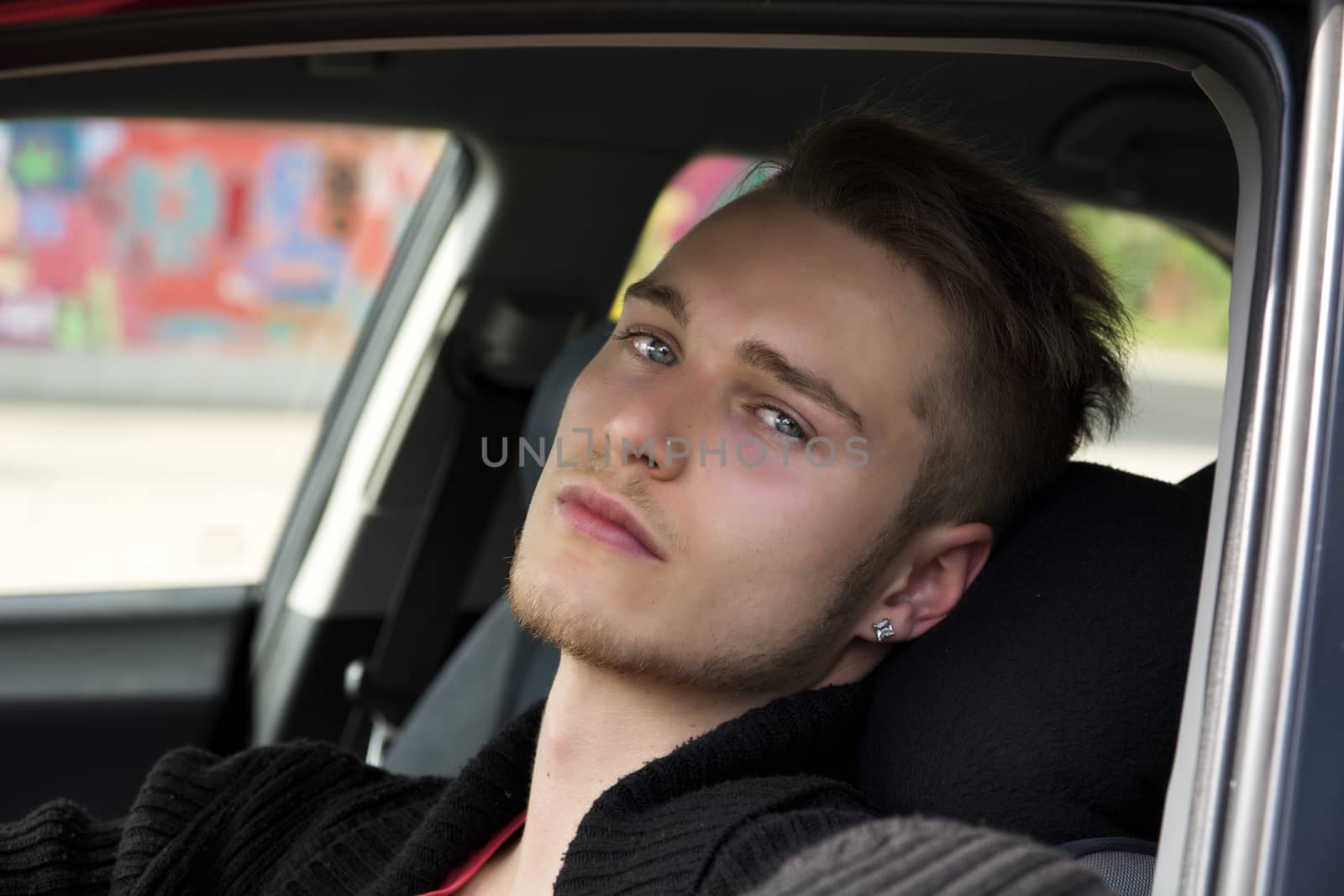 Handsome blond young man sitting in his car, looking at camera