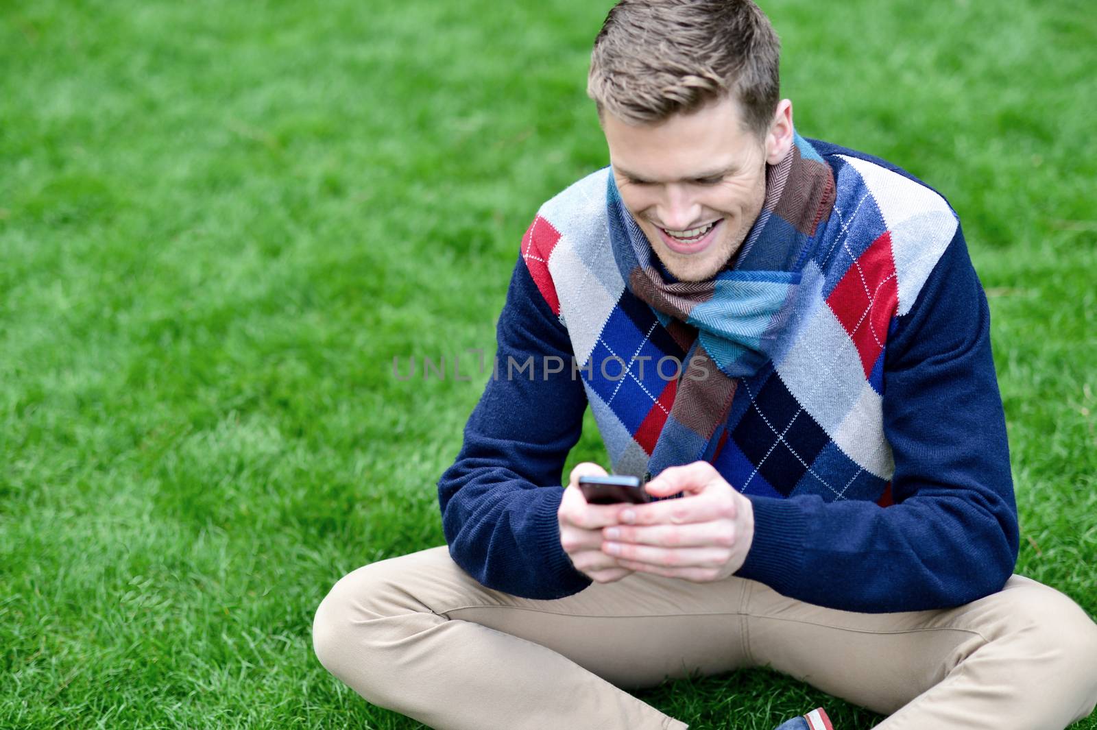 Cheerful young relaxed guy using mobile phone by stockyimages