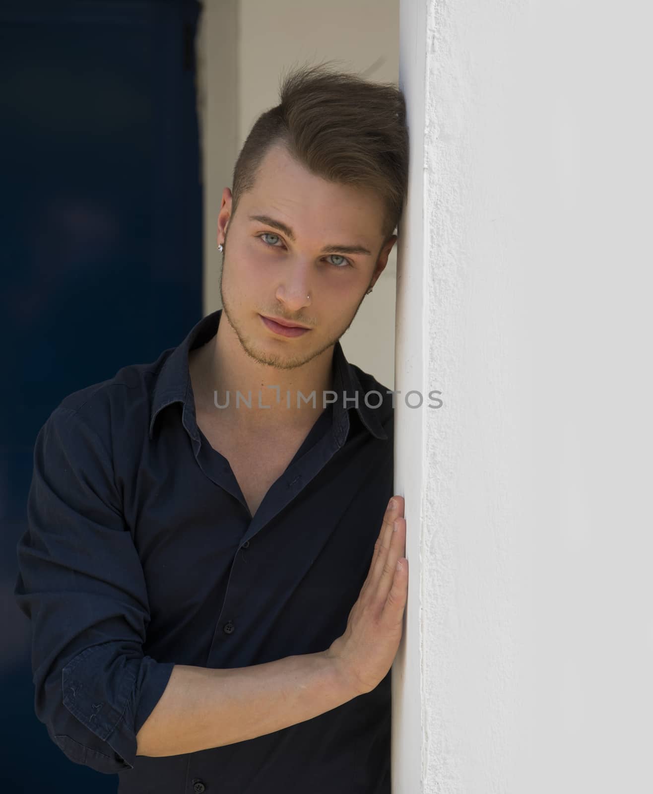 Attractive young blond man leaning against wall, looking at camera