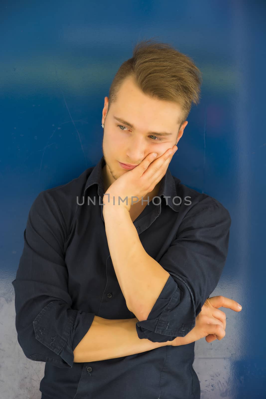 Attractive young man thinking, looking up with hand on his cheek on blue background