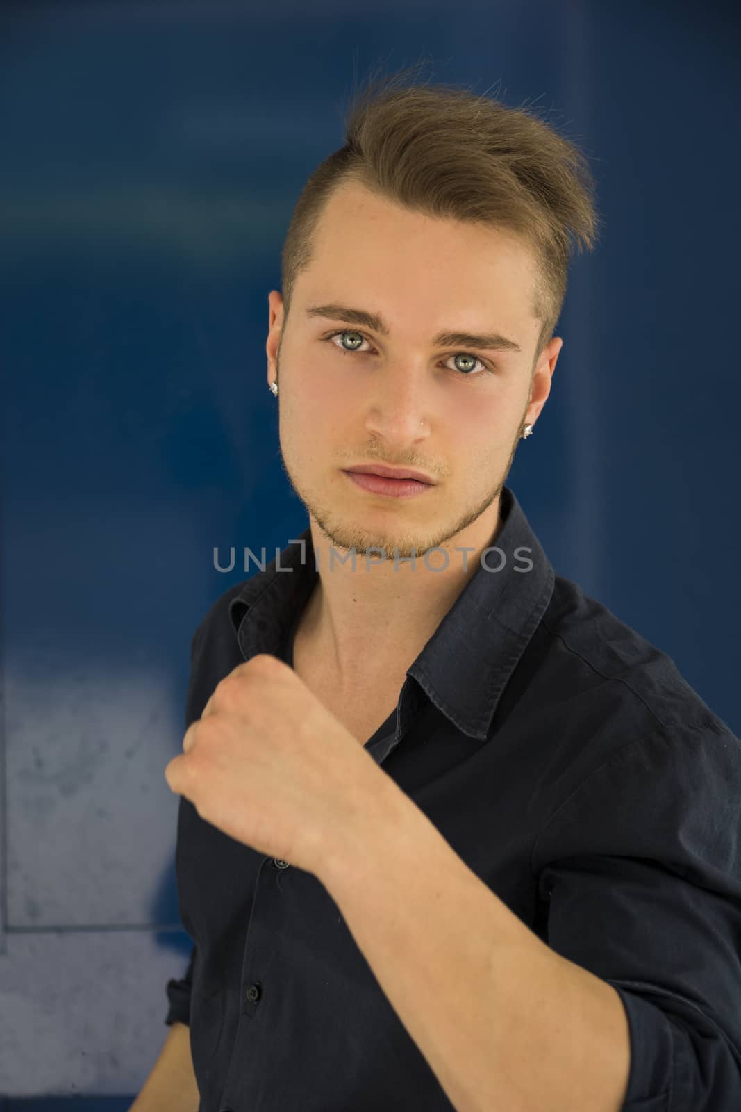 Handsome young man with aggressive expression of challenge, on blue background