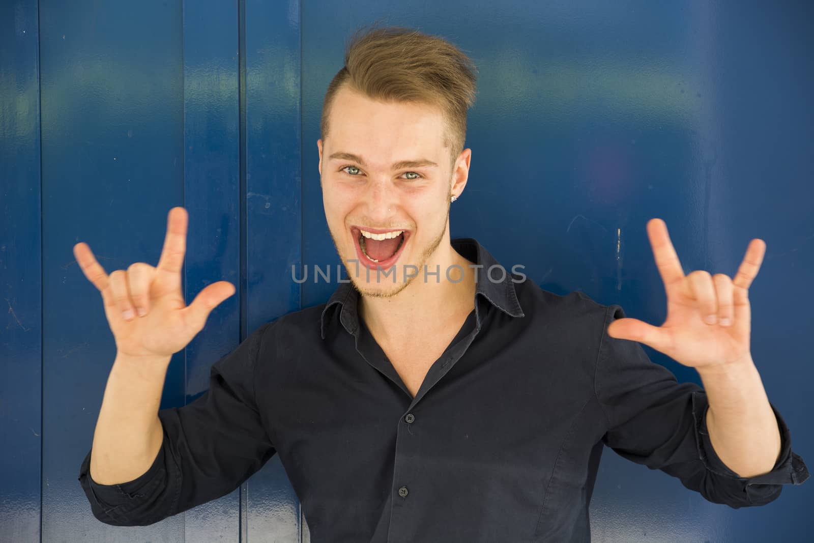 Happy handsome young man screaming and doing I Love You hand sign