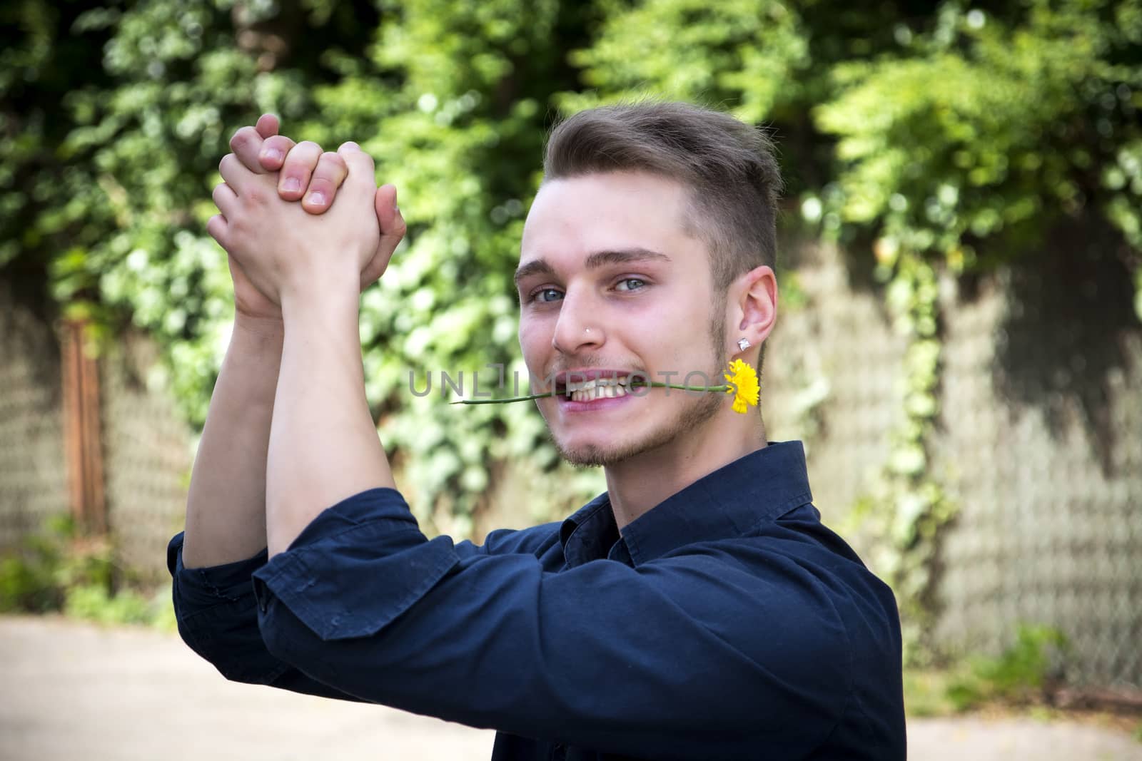 Handsome young man with flower in mouth clapping. Outdoors