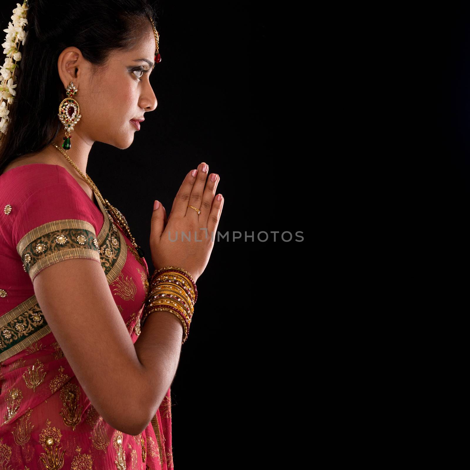 Beautiful Indian girl in greeting pose, traditional sari prayer isolated on black background with copy space on side.